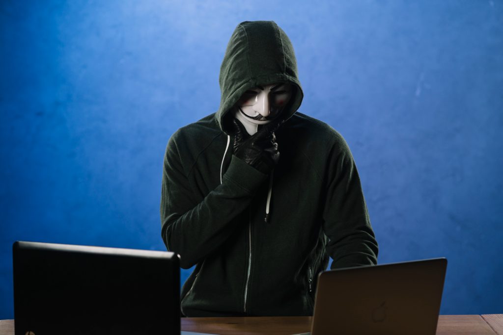 Masked hacker blocked by blockchain identity security stopping identity theft on laptop.