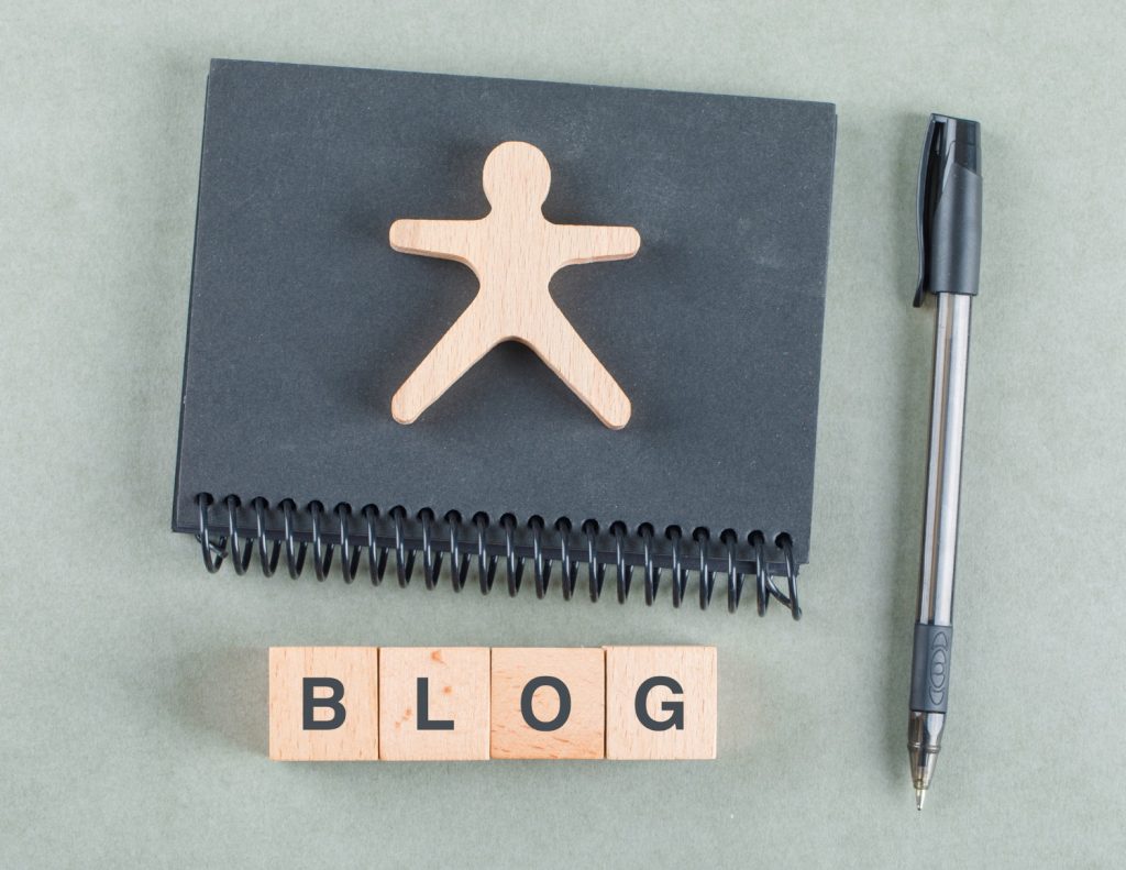 Blog notes concept with wooden blocks, pen and black notebook top view. How to use AI for blogging